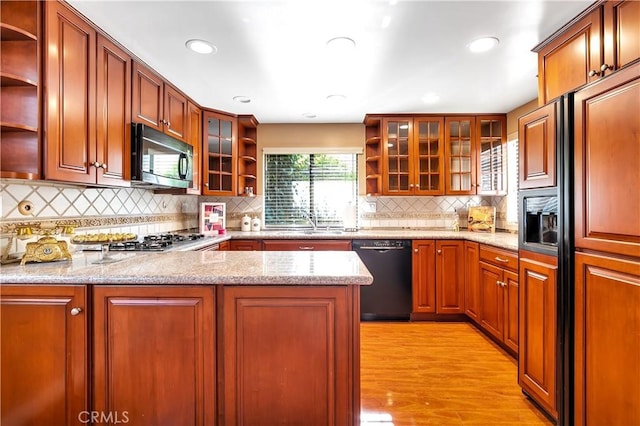 kitchen with light wood-style floors, light stone countertops, black appliances, and open shelves