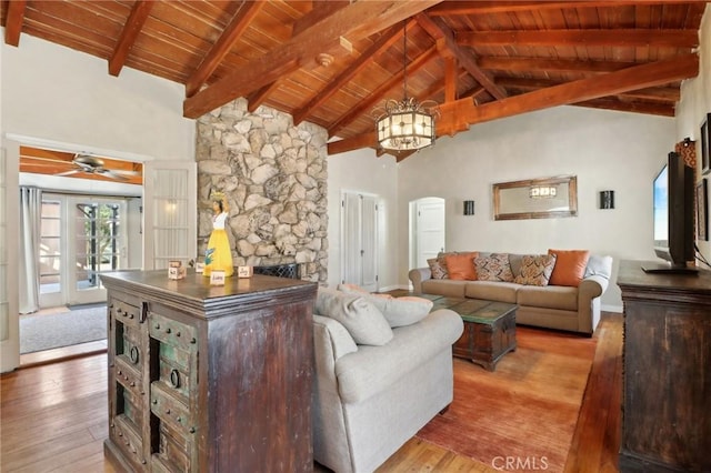 living room featuring beam ceiling, light hardwood / wood-style flooring, a stone fireplace, and high vaulted ceiling