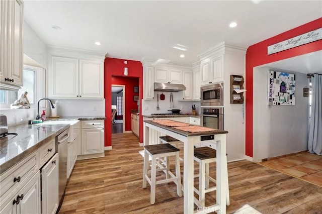 kitchen with white cabinets, appliances with stainless steel finishes, sink, a kitchen breakfast bar, and light wood-type flooring