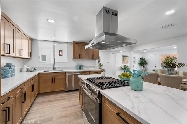 kitchen with appliances with stainless steel finishes, island range hood, light stone counters, and sink