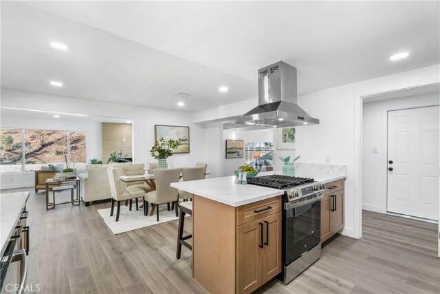 kitchen featuring light stone countertops, gas stove, a kitchen bar, light hardwood / wood-style floors, and island range hood