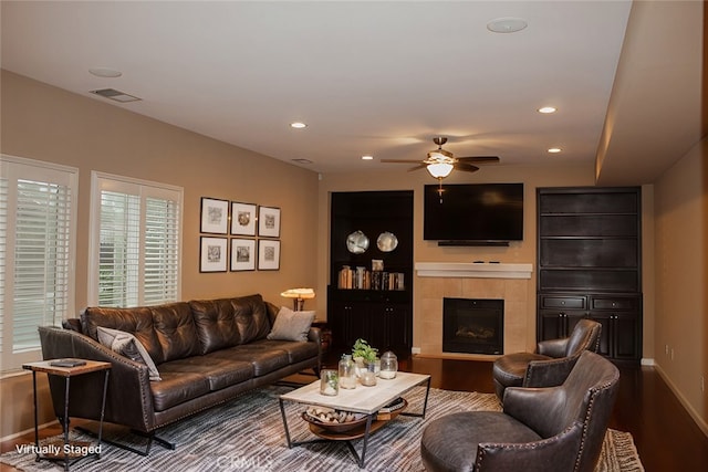 living room featuring hardwood / wood-style flooring, ceiling fan, and a tiled fireplace