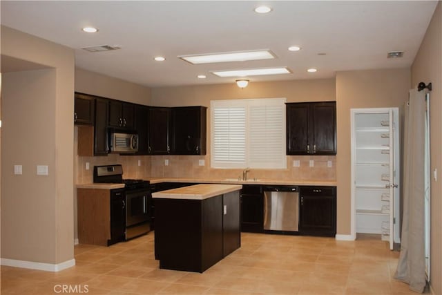 kitchen with light tile patterned floors, appliances with stainless steel finishes, backsplash, a center island, and sink