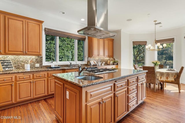 kitchen featuring decorative light fixtures, an inviting chandelier, an island with sink, ornamental molding, and island range hood