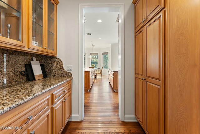 bar featuring crown molding, hanging light fixtures, light wood-type flooring, stone counters, and decorative backsplash