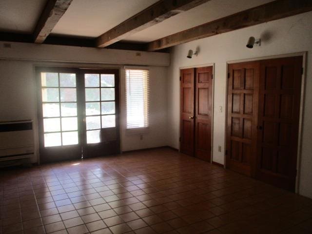 empty room with beam ceiling, tile patterned flooring, a wealth of natural light, and french doors