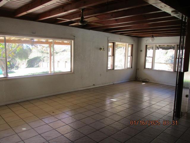 spare room featuring light tile patterned flooring, plenty of natural light, and beamed ceiling