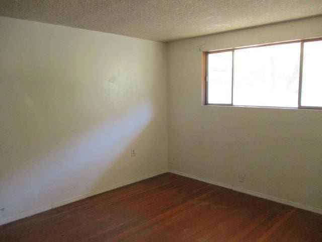 unfurnished room with a textured ceiling and dark wood-type flooring