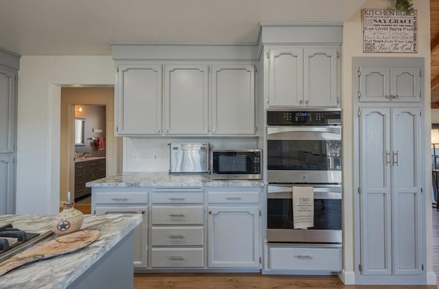 kitchen with stainless steel appliances, white cabinetry, and light stone countertops