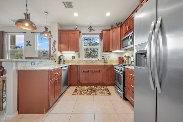 kitchen featuring light tile patterned floors, kitchen peninsula, appliances with stainless steel finishes, decorative light fixtures, and light stone counters