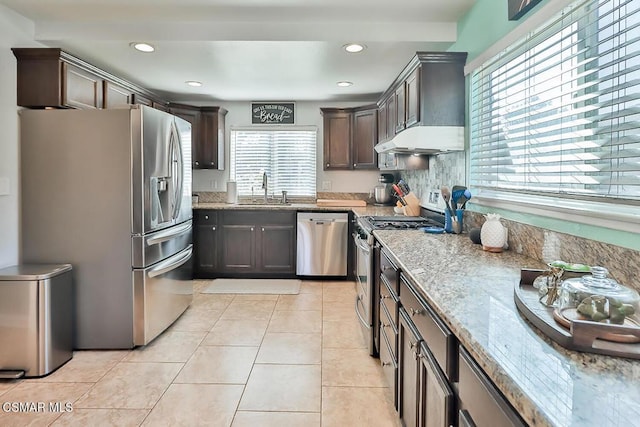 kitchen with sink, dark brown cabinetry, light stone countertops, stainless steel appliances, and light tile patterned floors