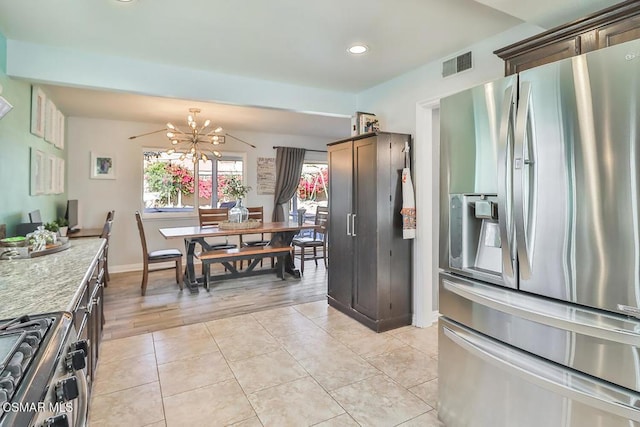 kitchen featuring appliances with stainless steel finishes, light tile patterned flooring, light stone countertops, a chandelier, and dark brown cabinetry