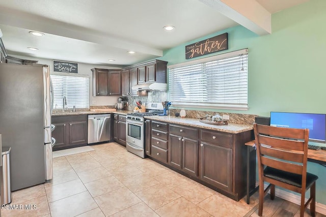 kitchen with beam ceiling, appliances with stainless steel finishes, light stone counters, and dark brown cabinets