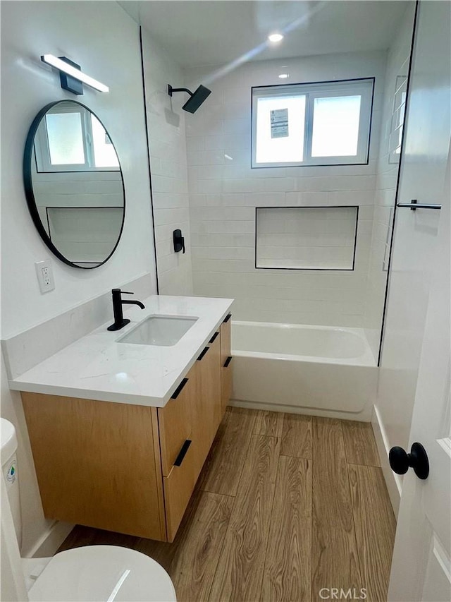 full bathroom featuring tiled shower / bath combo, wood-type flooring, vanity, and a healthy amount of sunlight