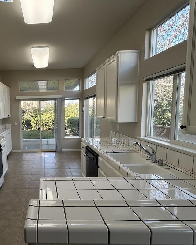 kitchen featuring white cabinets, a wealth of natural light, black dishwasher, and tile countertops