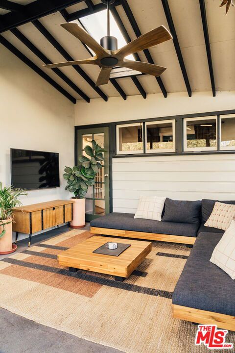 carpeted living room with ceiling fan, wood walls, and lofted ceiling with beams