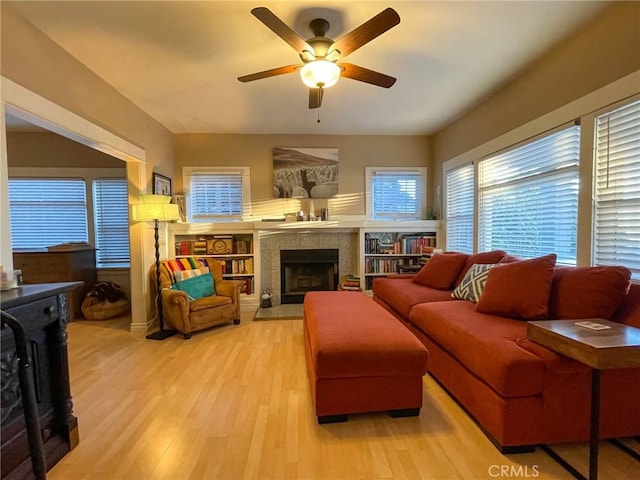 living room featuring ceiling fan, light hardwood / wood-style flooring, and a tiled fireplace