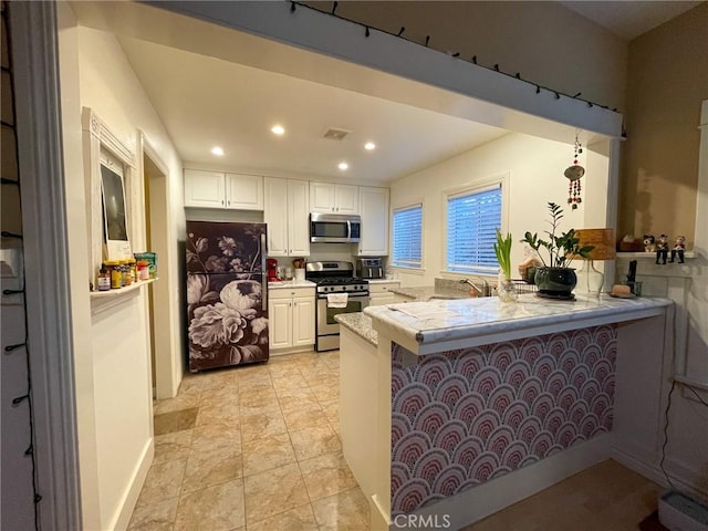 kitchen with kitchen peninsula, appliances with stainless steel finishes, white cabinetry, and a breakfast bar area