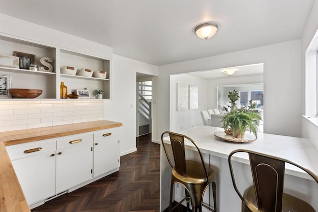 kitchen with white cabinets, decorative backsplash, butcher block counters, and dark parquet floors