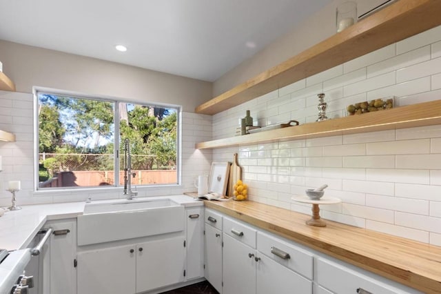 kitchen with butcher block countertops, decorative backsplash, sink, white cabinetry, and stainless steel range