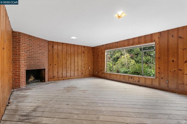 unfurnished living room featuring a brick fireplace, light wood-type flooring, and wood walls