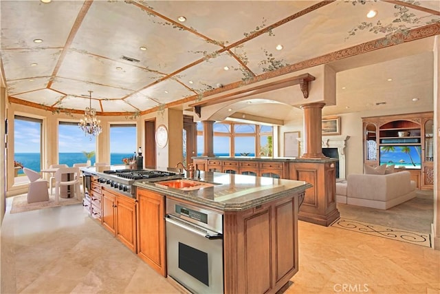 kitchen with stainless steel appliances, a water view, ornate columns, and a center island with sink