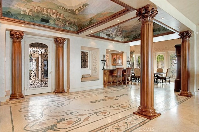 entrance foyer featuring decorative columns, crown molding, indoor bar, and a towering ceiling