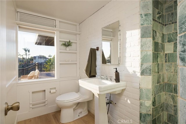 bathroom with tiled shower, toilet, and wood finished floors