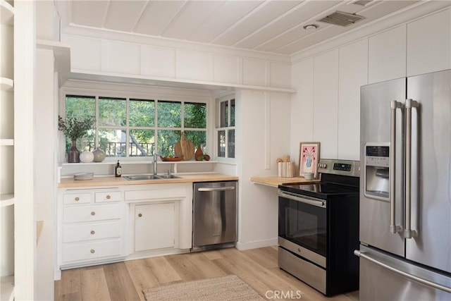 kitchen with appliances with stainless steel finishes, crown molding, light wood-type flooring, white cabinetry, and a sink