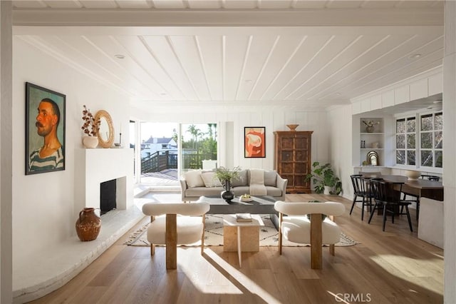 living area with a fireplace with raised hearth, built in shelves, wooden ceiling, wood finished floors, and crown molding