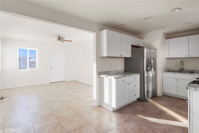 kitchen with stainless steel fridge, ceiling fan, light tile patterned flooring, white cabinets, and sink