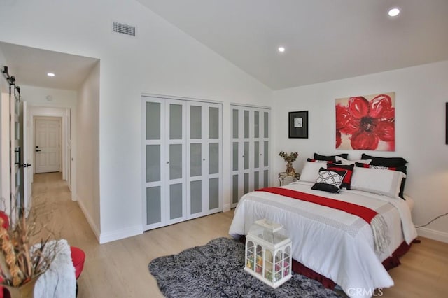 bedroom with a barn door, light hardwood / wood-style flooring, and high vaulted ceiling