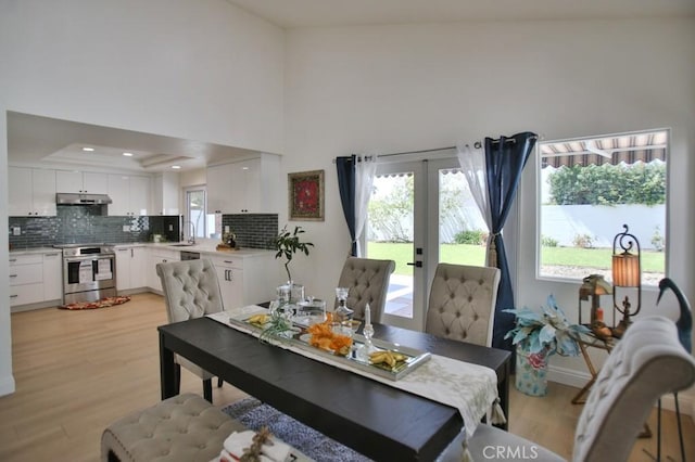 dining space featuring a towering ceiling, light hardwood / wood-style flooring, a raised ceiling, and french doors