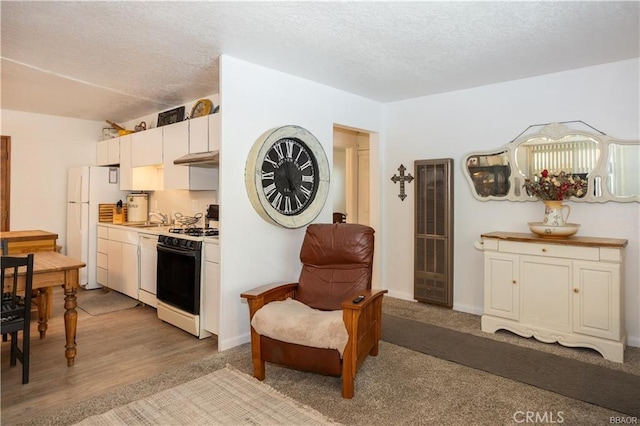 kitchen featuring white appliances, white cabinets, a textured ceiling, sink, and light wood-type flooring