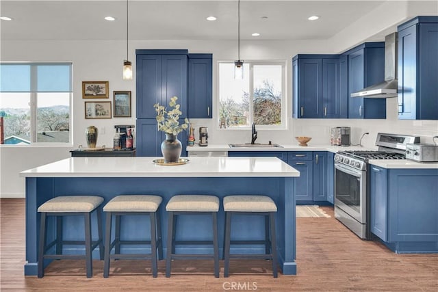 kitchen featuring a breakfast bar, stainless steel range with gas cooktop, blue cabinetry, a sink, and wall chimney exhaust hood