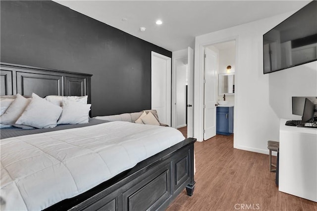 bedroom with recessed lighting, connected bathroom, baseboards, and wood finished floors