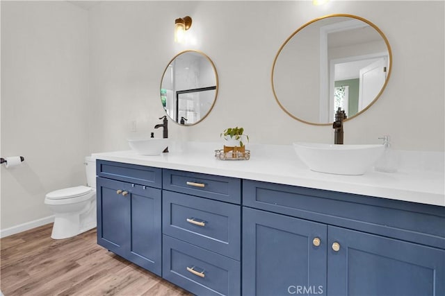 full bath with double vanity, a sink, toilet, and wood finished floors