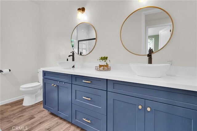 full bathroom featuring double vanity, a sink, wood finished floors, and toilet