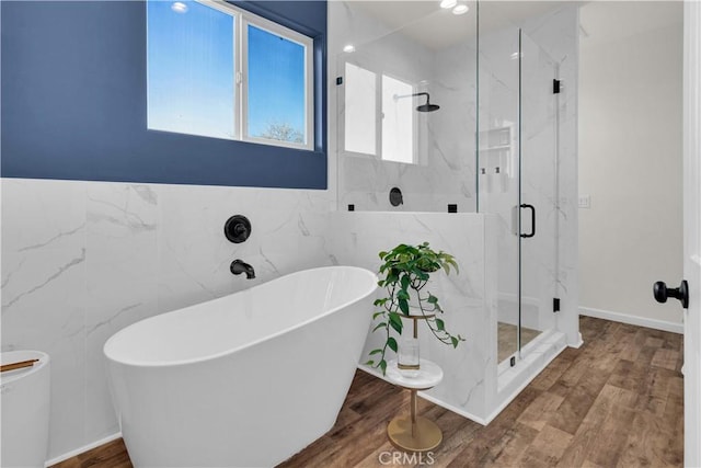 full bathroom featuring a freestanding bath, wood finished floors, a marble finish shower, and tile walls