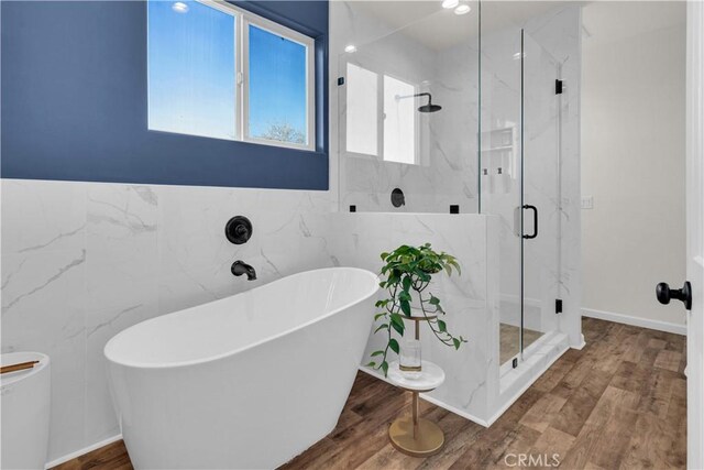 full bathroom featuring a soaking tub, tile walls, a marble finish shower, and wood finished floors