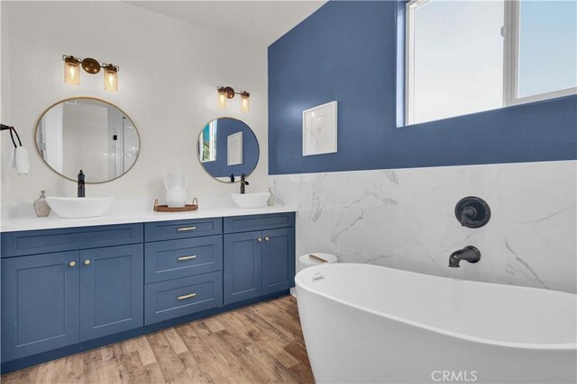 bathroom with a freestanding tub, double vanity, a sink, and wood finished floors