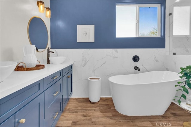 full bath with tile walls, double vanity, a sink, wood finished floors, and a freestanding tub