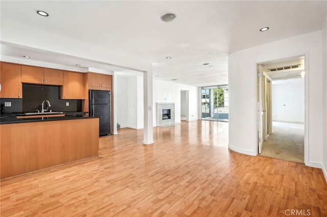 kitchen featuring a tile fireplace, black refrigerator, sink, backsplash, and light hardwood / wood-style floors