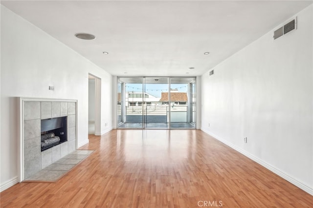 unfurnished living room with a wall of windows, light hardwood / wood-style floors, and a tile fireplace