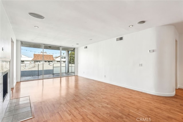 unfurnished living room with floor to ceiling windows, a fireplace, and light hardwood / wood-style flooring