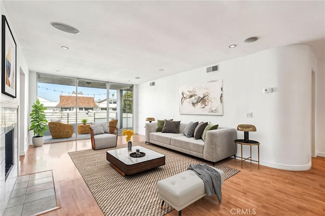 living room featuring a tile fireplace, a wall of windows, and light hardwood / wood-style flooring