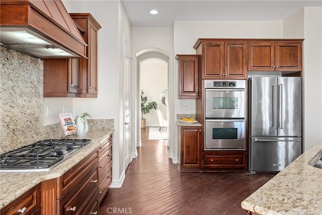 kitchen featuring tasteful backsplash, dark wood-type flooring, light stone counters, stainless steel appliances, and custom range hood