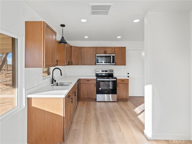 kitchen with decorative light fixtures, light wood-type flooring, appliances with stainless steel finishes, and sink