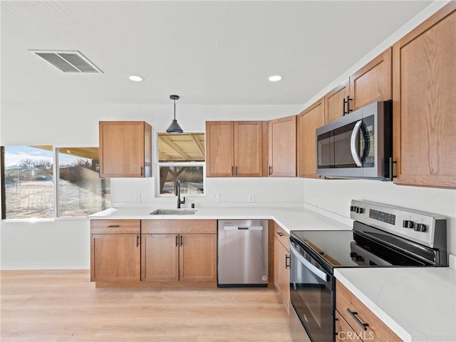 kitchen with light stone countertops, stainless steel appliances, sink, hanging light fixtures, and light hardwood / wood-style flooring