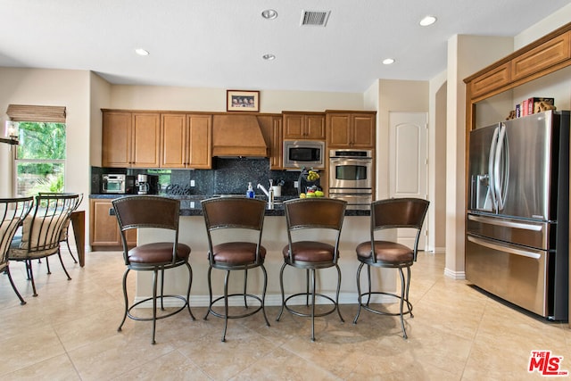 kitchen featuring wall chimney range hood, a center island with sink, a kitchen bar, decorative backsplash, and stainless steel appliances